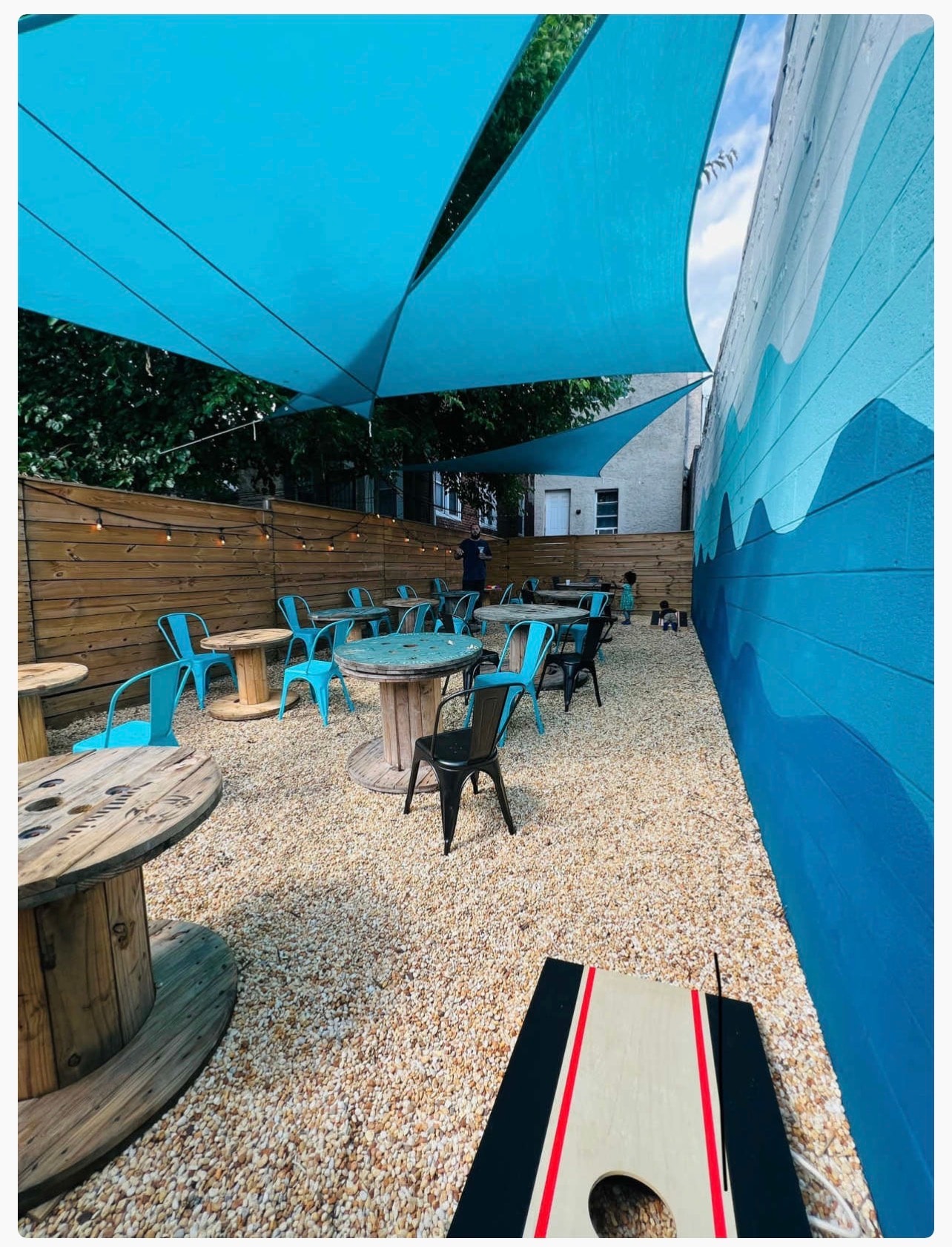 Durag Café patio with cornhole, string lights, and wave mural